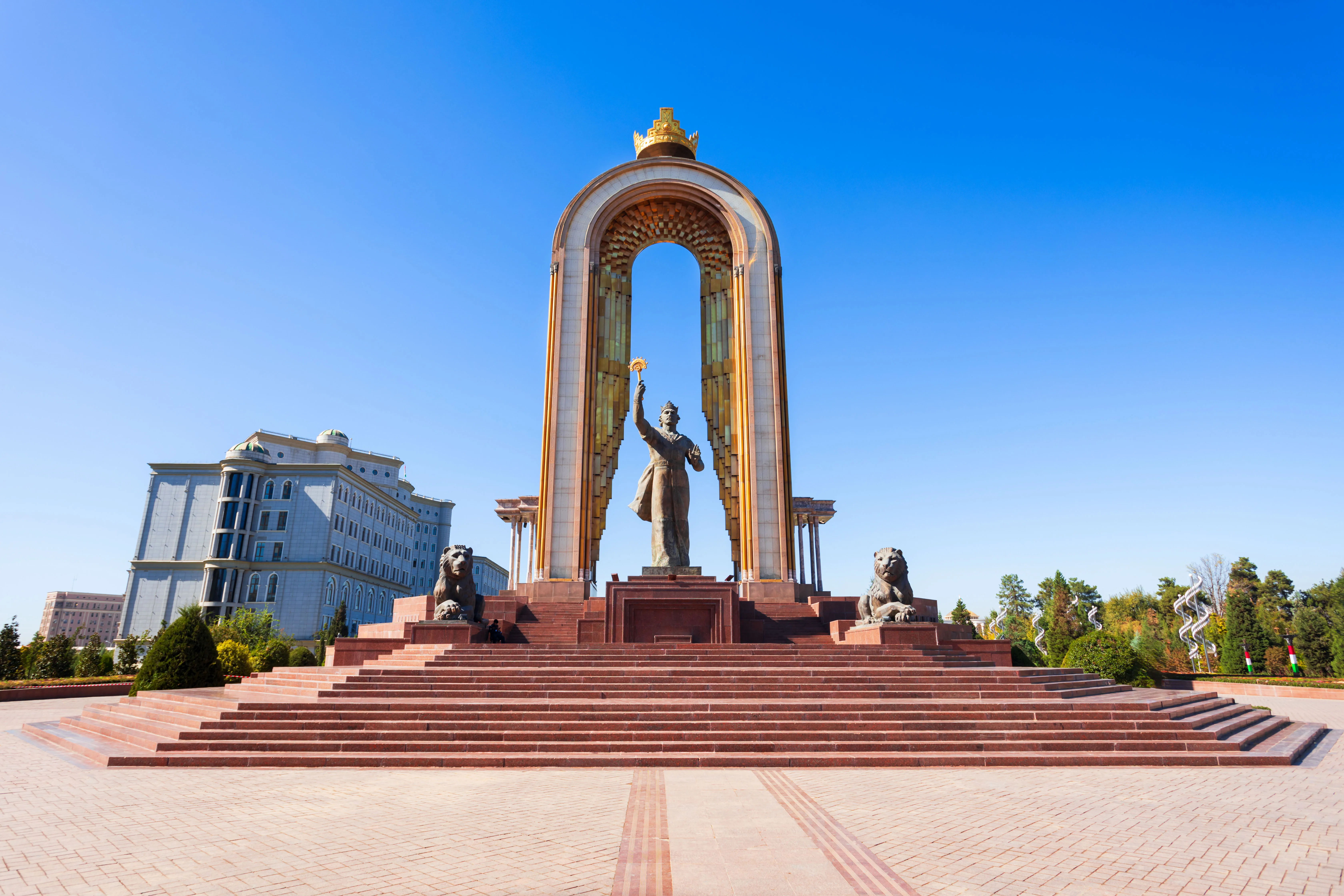 The Ismoil Somoni Monument in Dushanbe, Tajikistan, featuring a bronze statue under a large golden arch against a clear blue sky