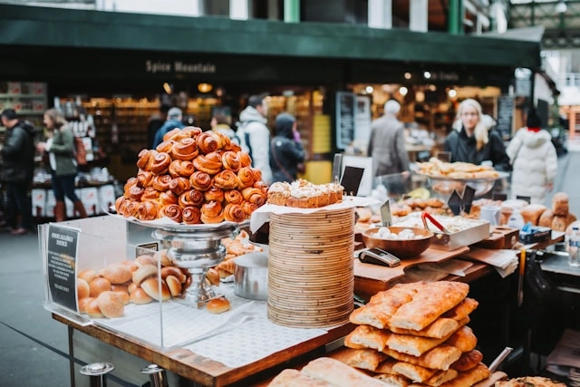a-table-full-of-bakery-with-people-walking-by