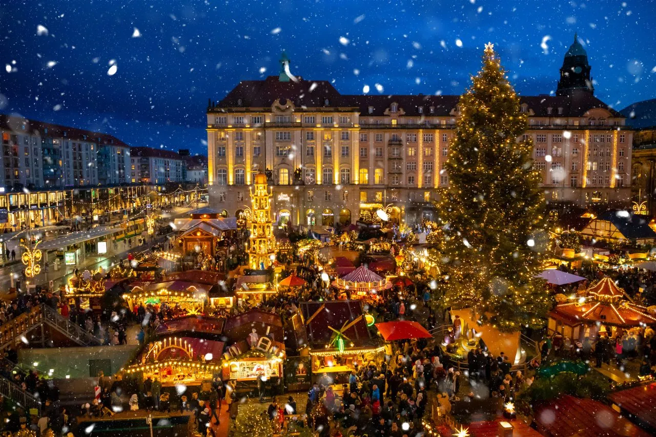 Large Christmas market square at night with a decorated tree and crowded stalls