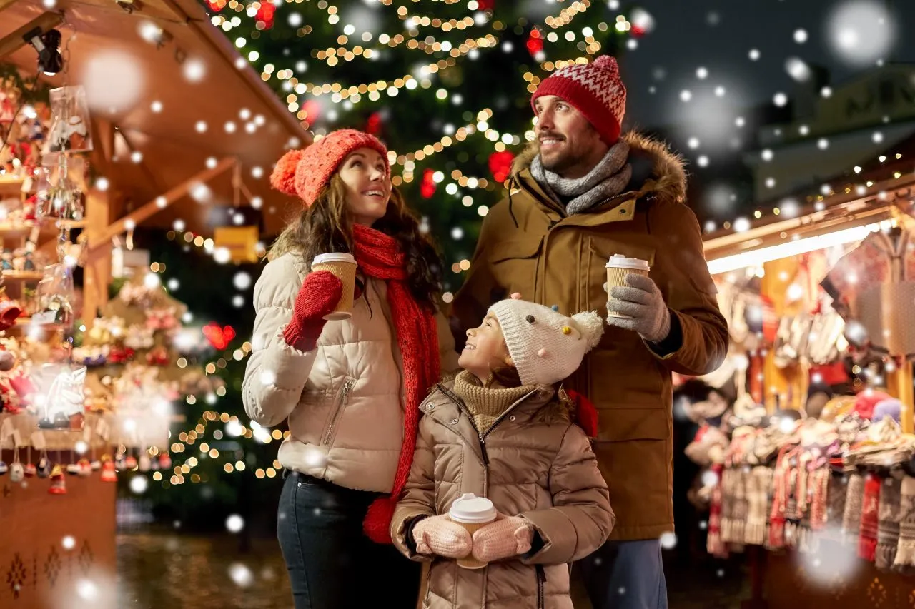 Family in winter clothing enjoying a festive Christmas market with lights and snow
