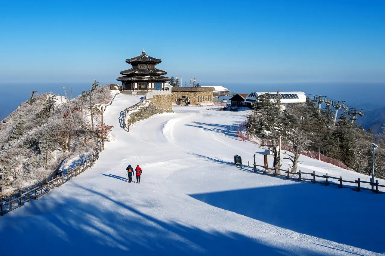 Snow-covered mountain path leading to a traditional pavilion overlooking the sea