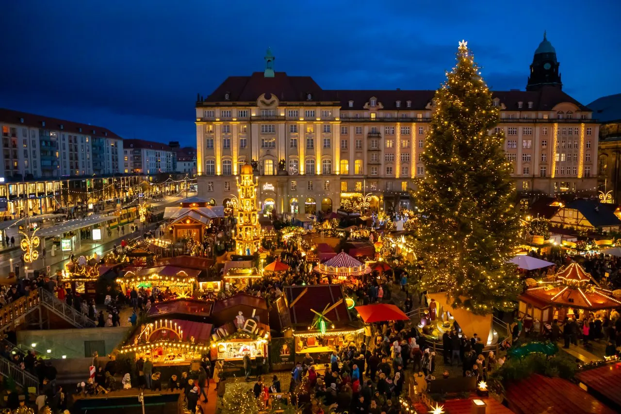 Large Christmas market square at night with a decorated tree and crowded stalls