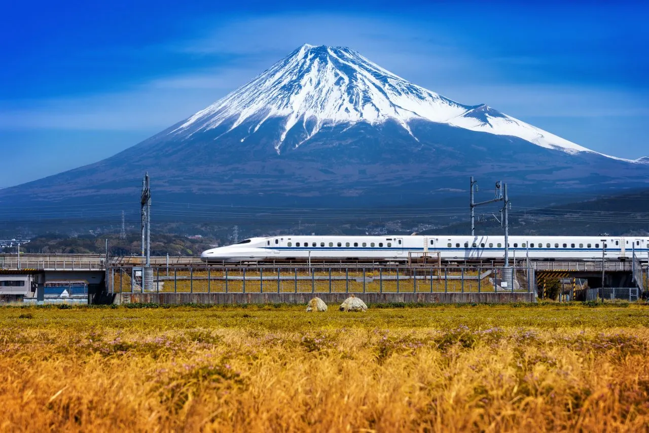 High-speed train passing in front of Mount Fuji with fields in the foreground
