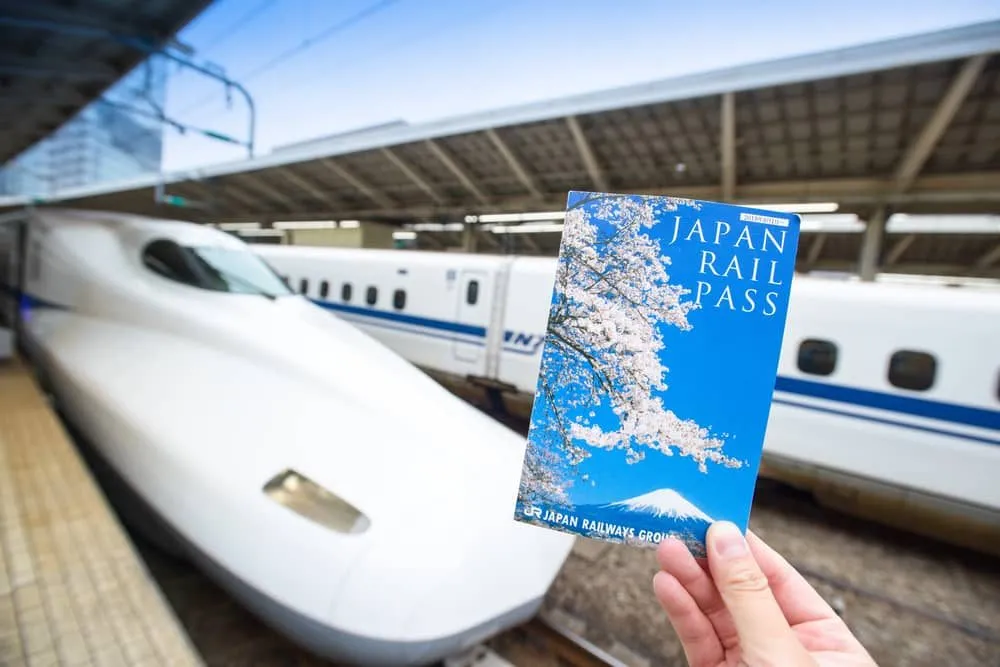 Hand holding a Japan Rail Pass ticket with a bullet train at the station