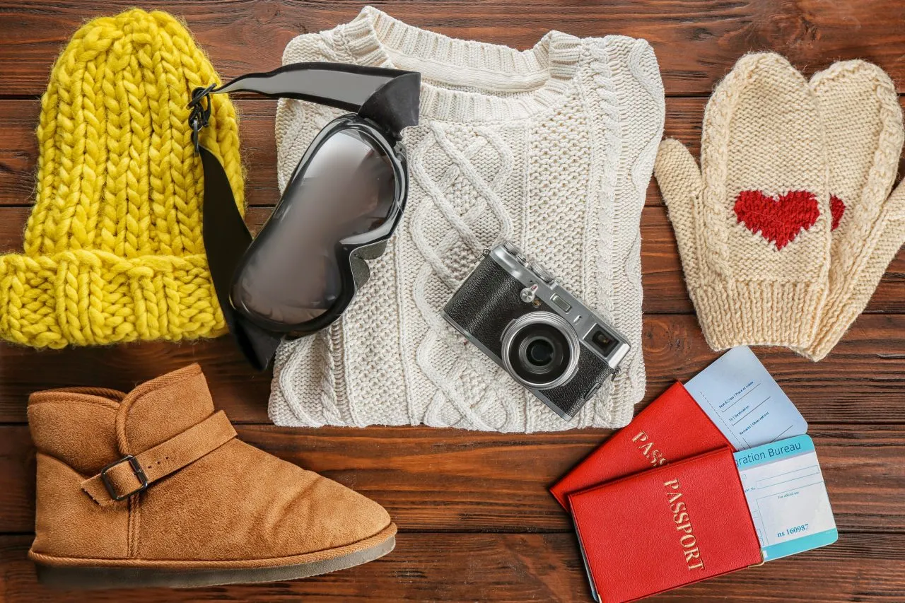 warm-clothes-with-ski-goggles-photo-camera-documents-wooden-background-winter-vacation-concept