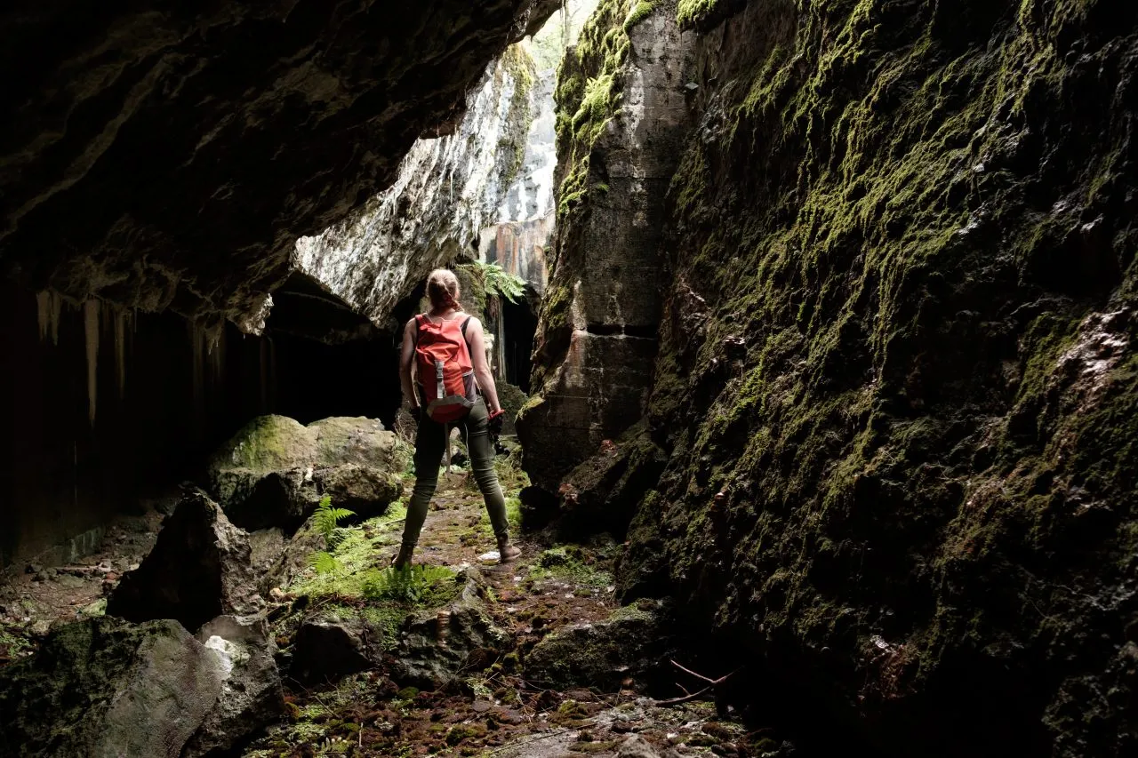 Explorer hiking through a moss-covered cave in Aokigahara Forest near Mount Fuji