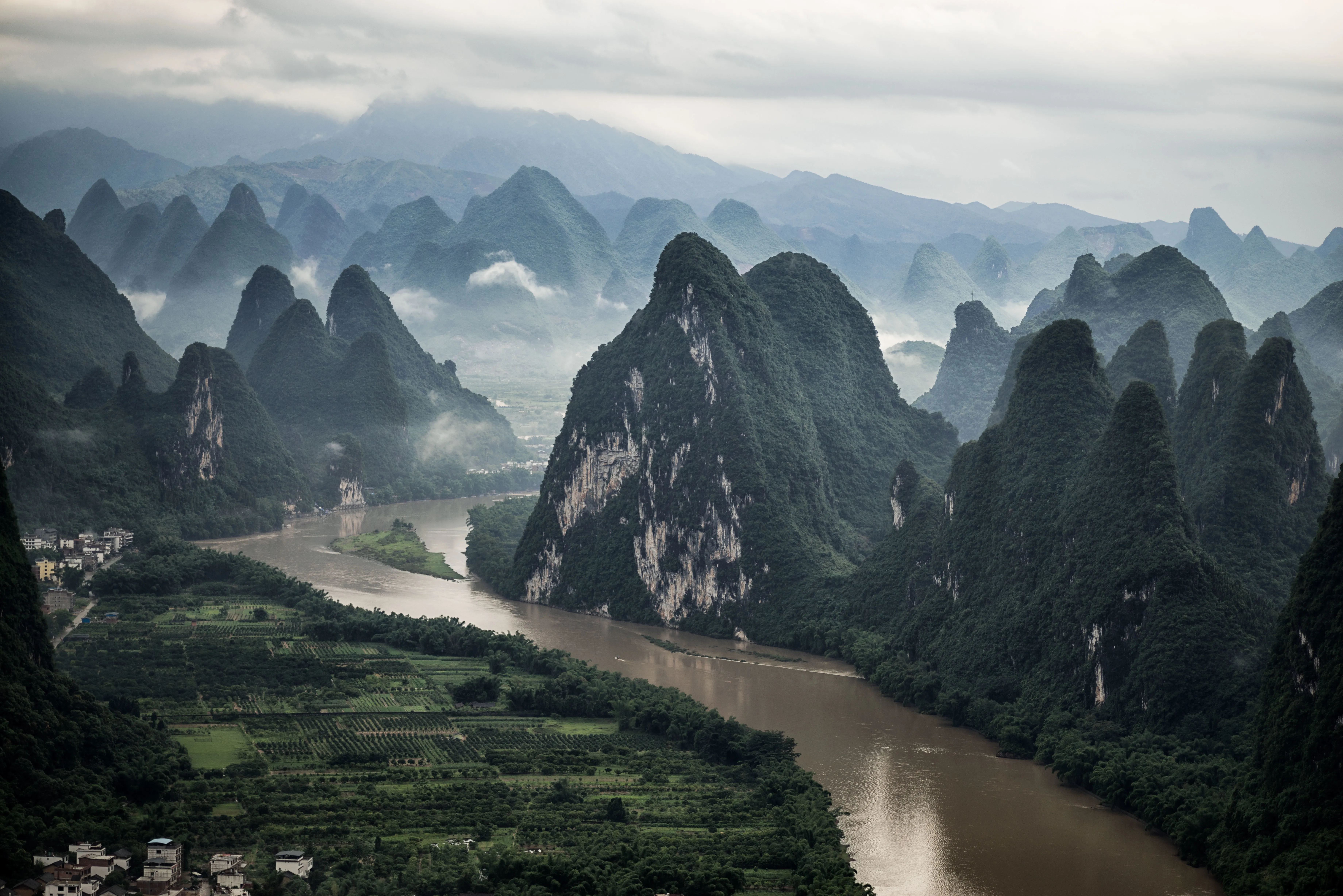 An elevated, wide-angle shot of the Li River winding through a dense cluster of dramatic, mist-covered karst mountains in Guangxi, China.