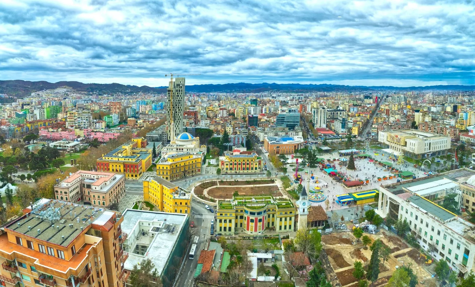 An aerial, high-angle panoramic shot overlooking Skanderbeg Square and the surrounding cityscape of Tirana, Albania.
