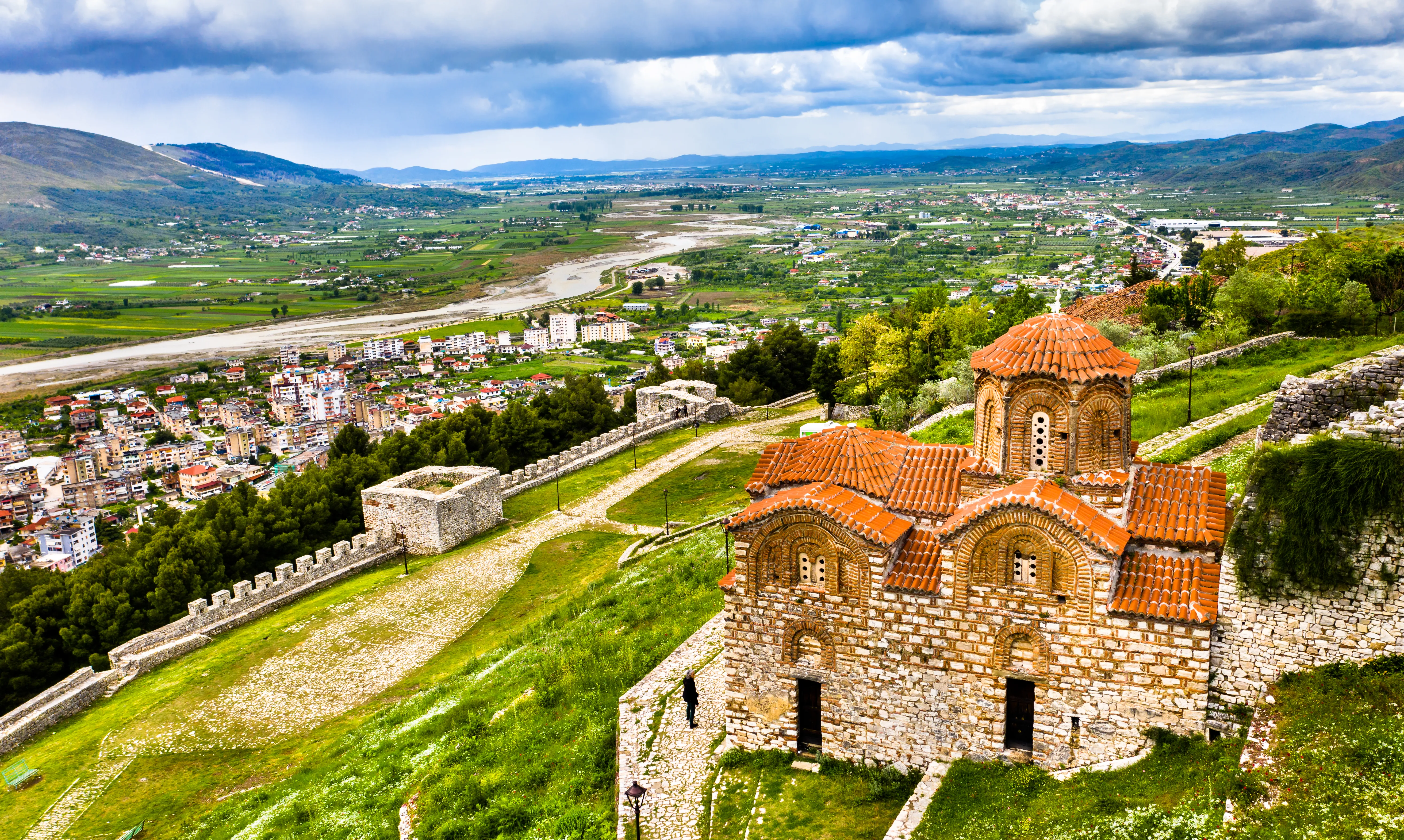 An aerial, high-angle panoramic shot of the Church of the Holy Trinity sitting within the stone walls of Berat Castle in Albania.