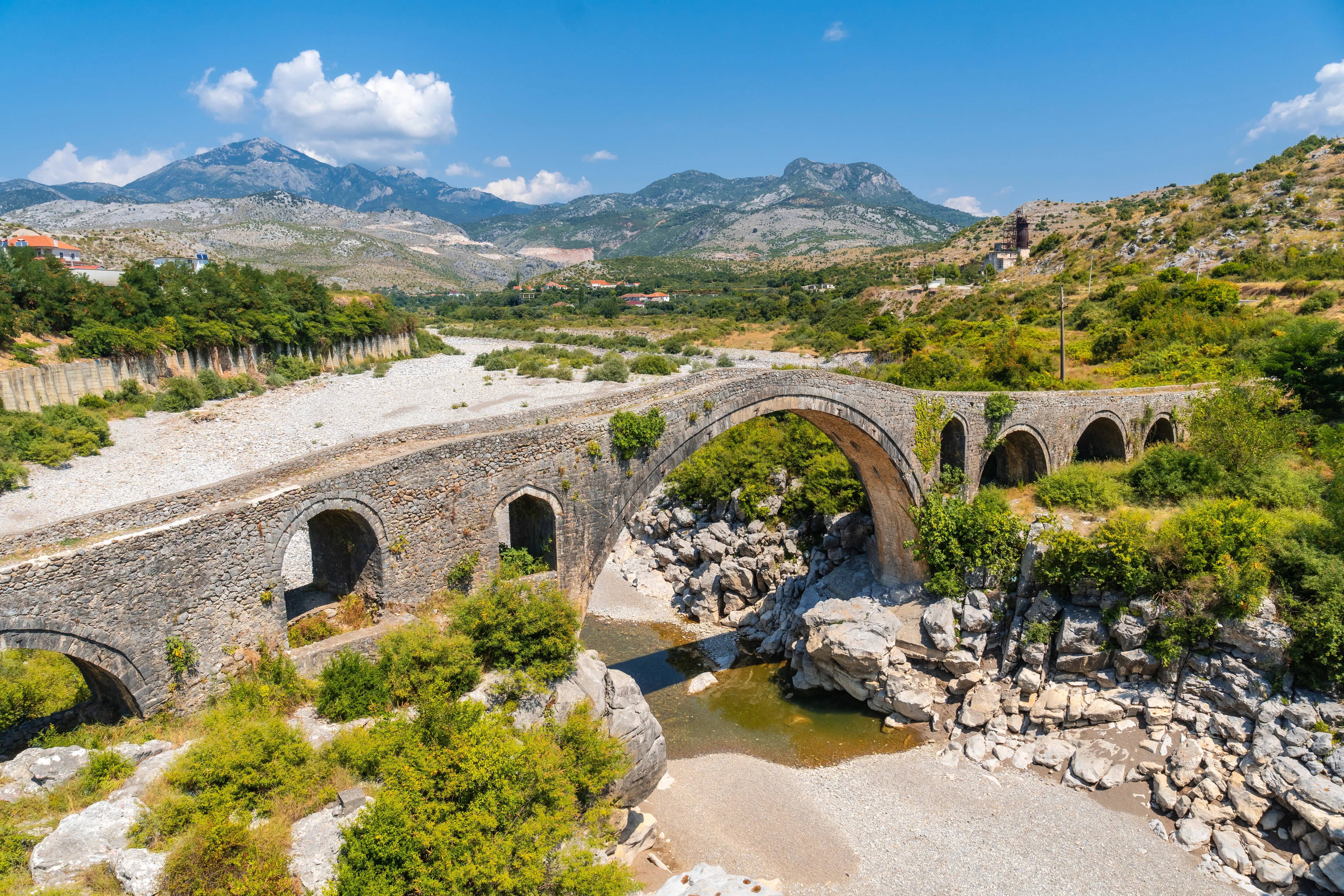 A wide-angle, elevated shot of the historic Mesi Bridge (Ura e Mesit) in Shkodër, Albania.