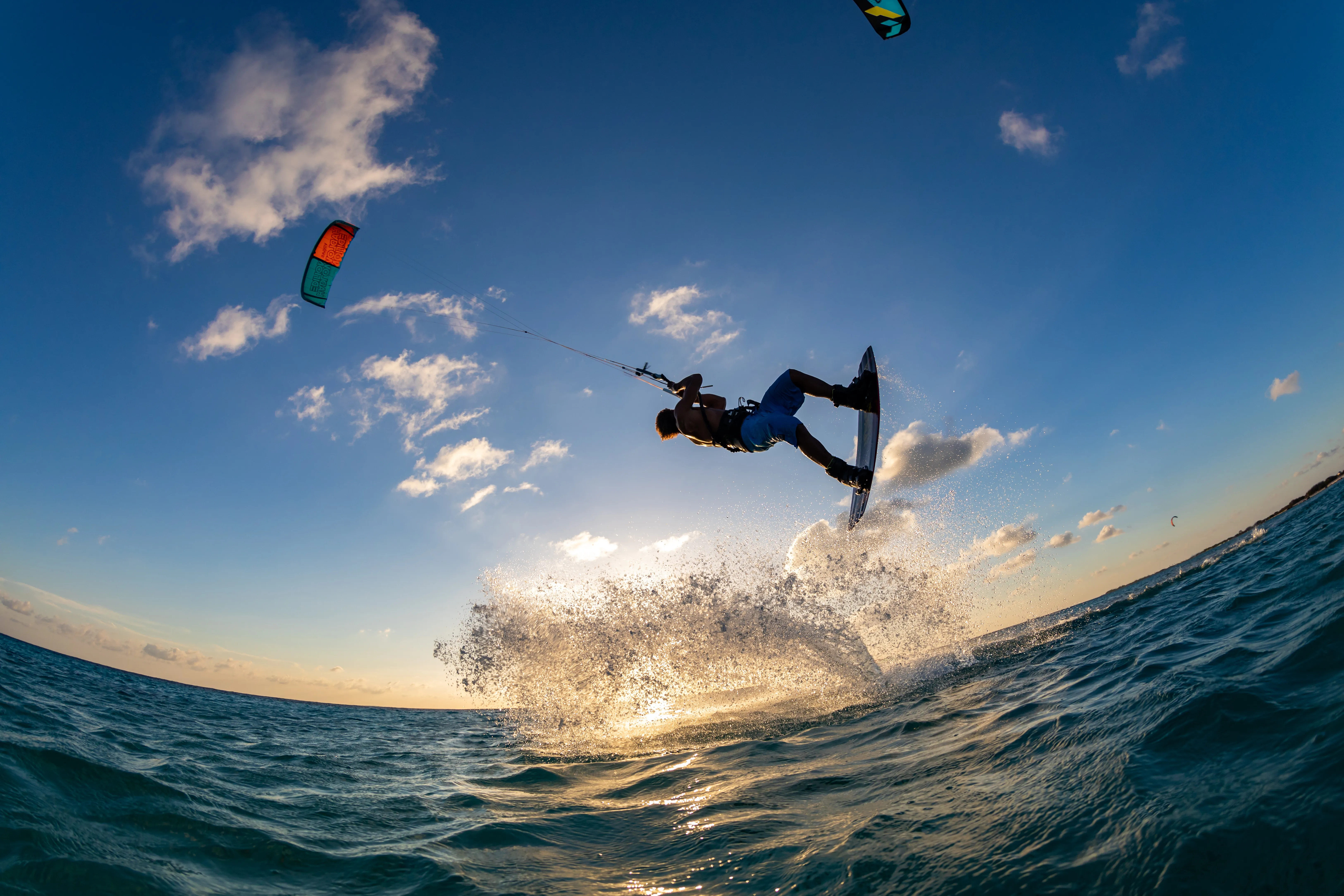Kitesurfer performing tricks over ocean waves during sunset in Maui