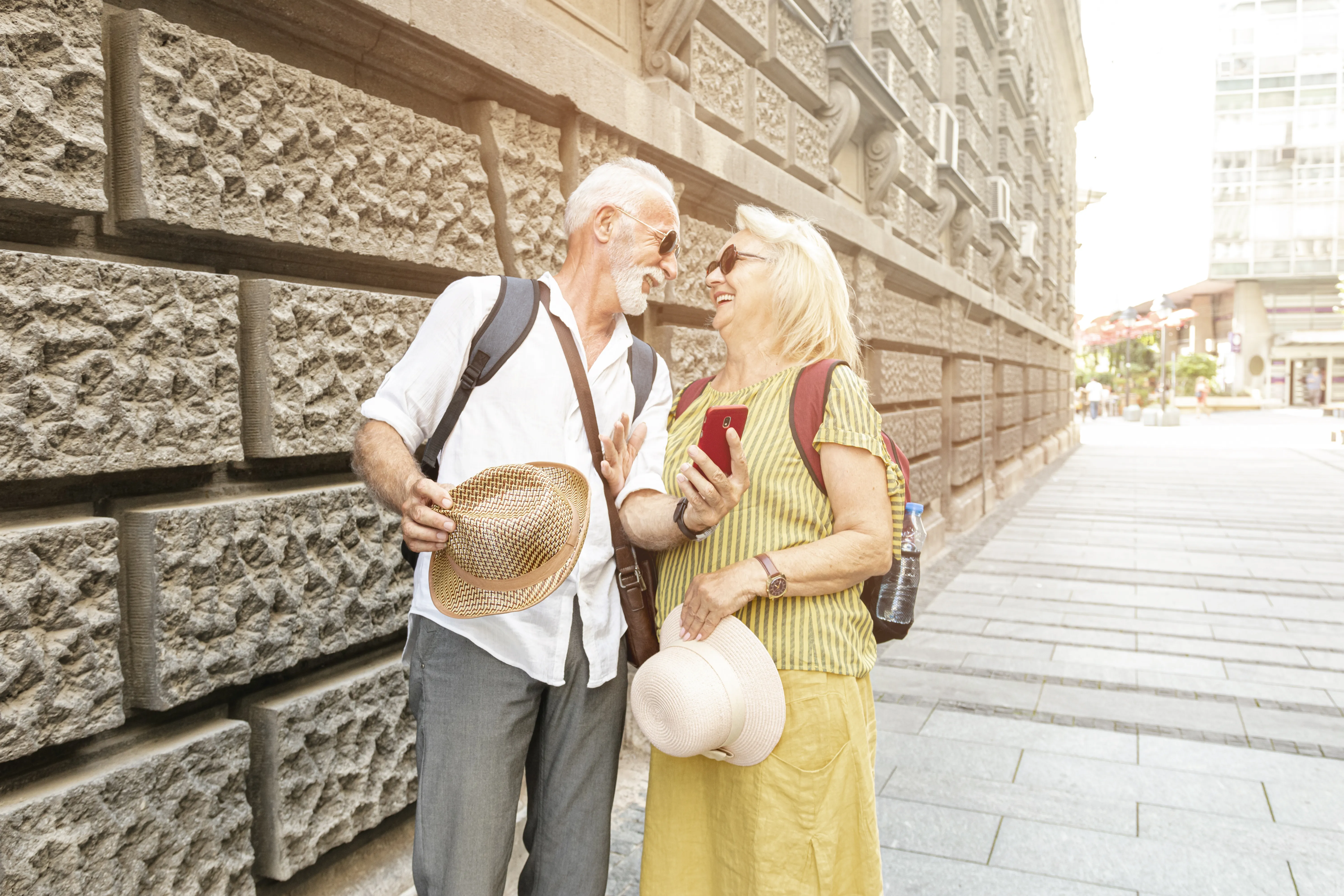 An elderly couple laughing and looking at a smartphone on a city street