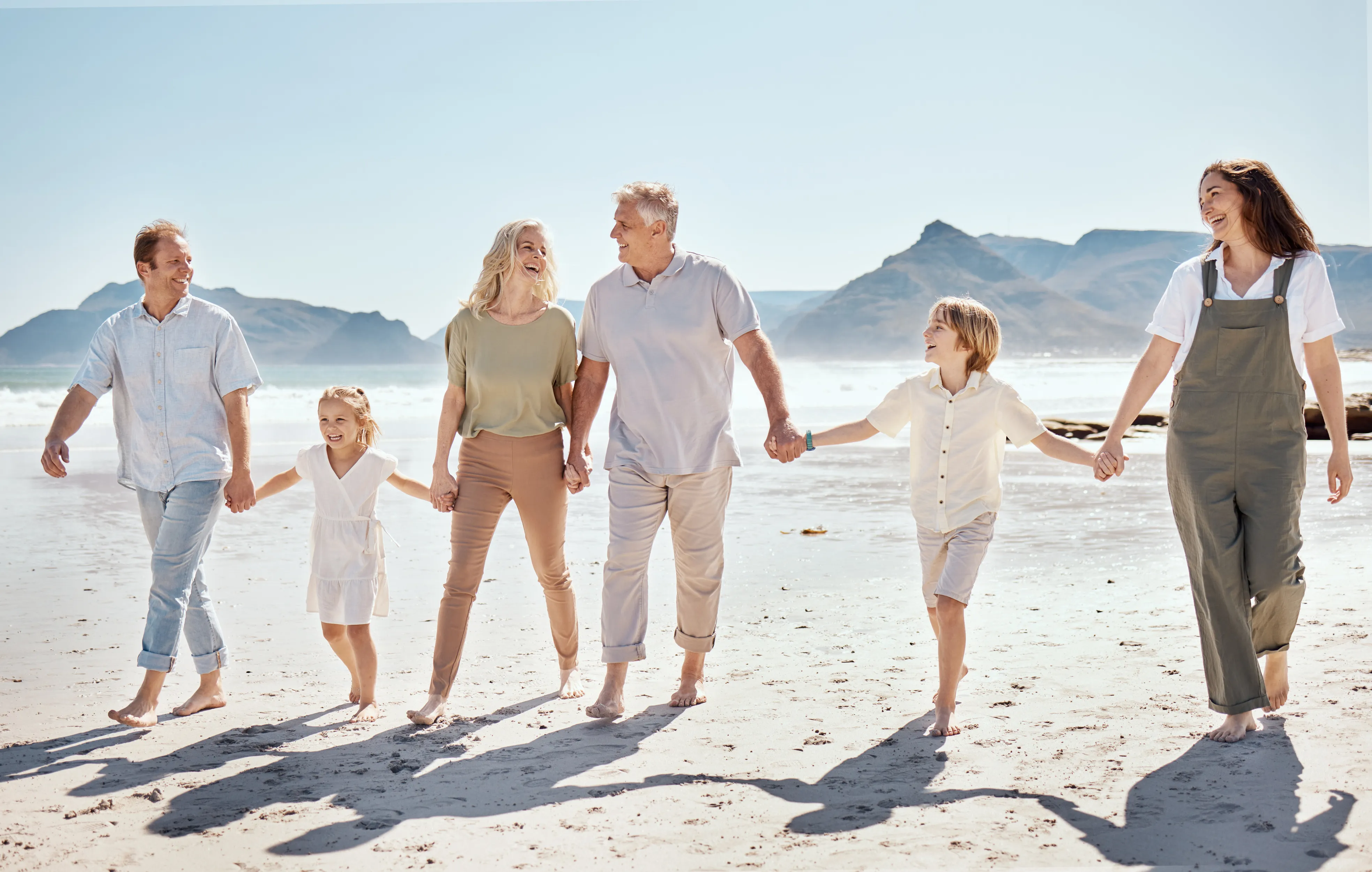 A multi-generational family walking hand-in-hand on a sandy beach.