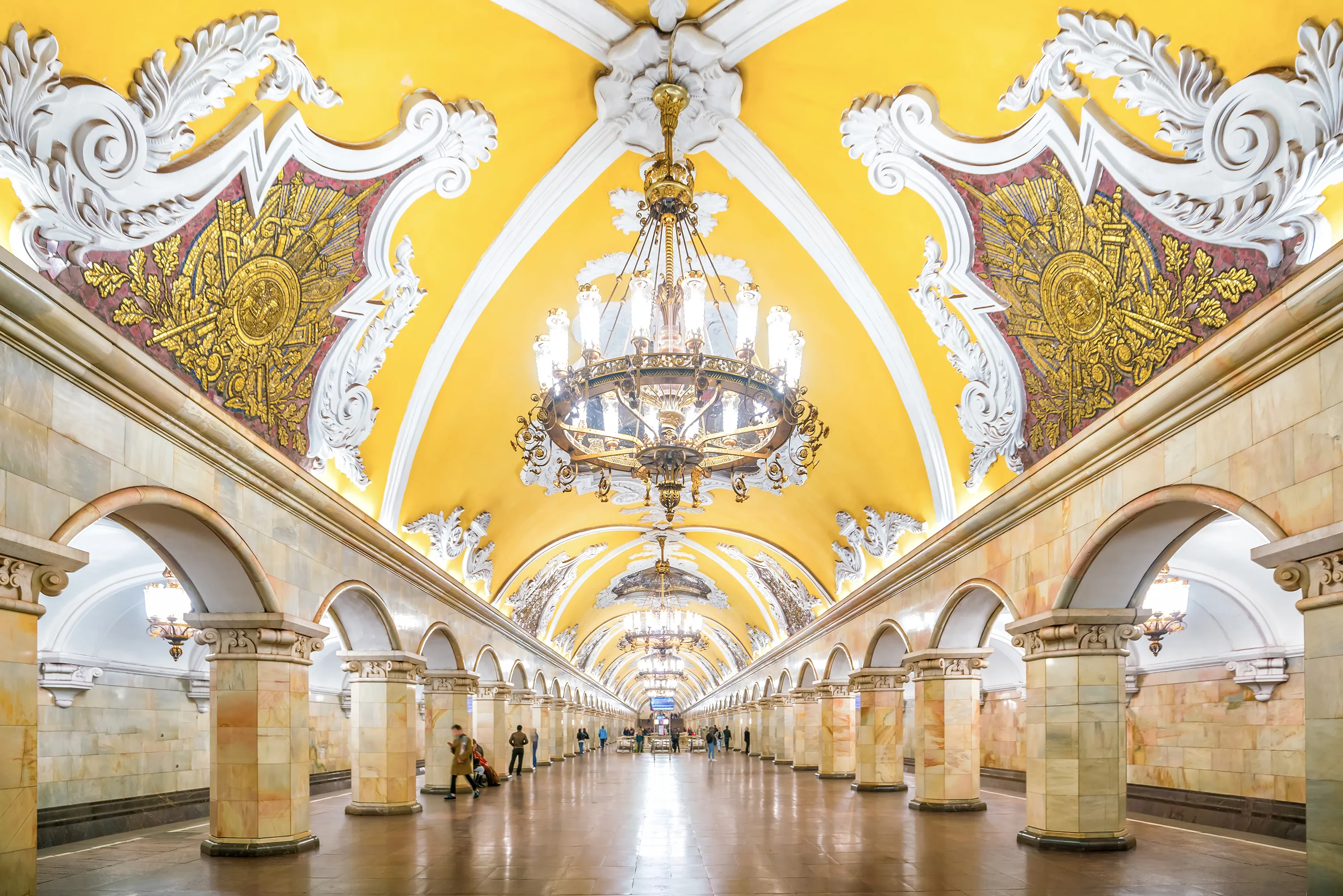 An interior photograph shows the opulent Baroque-style central platform hall of Komsomolskaya Metro Station in Moscow, Russia