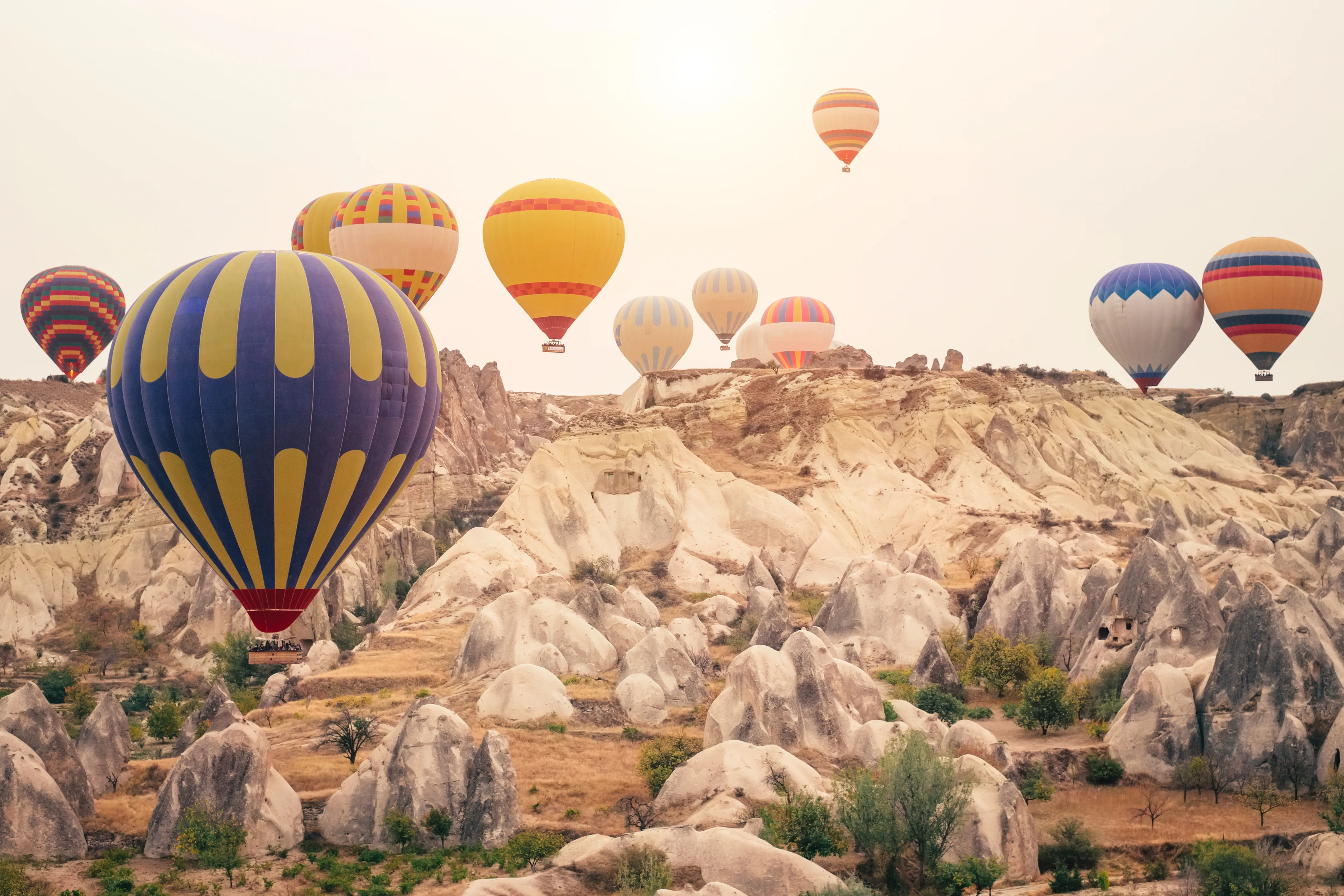 An aerial and landscape photograph shows numerous hot air balloons flying over the volcanic rock formations of Cappadocia, Turkey