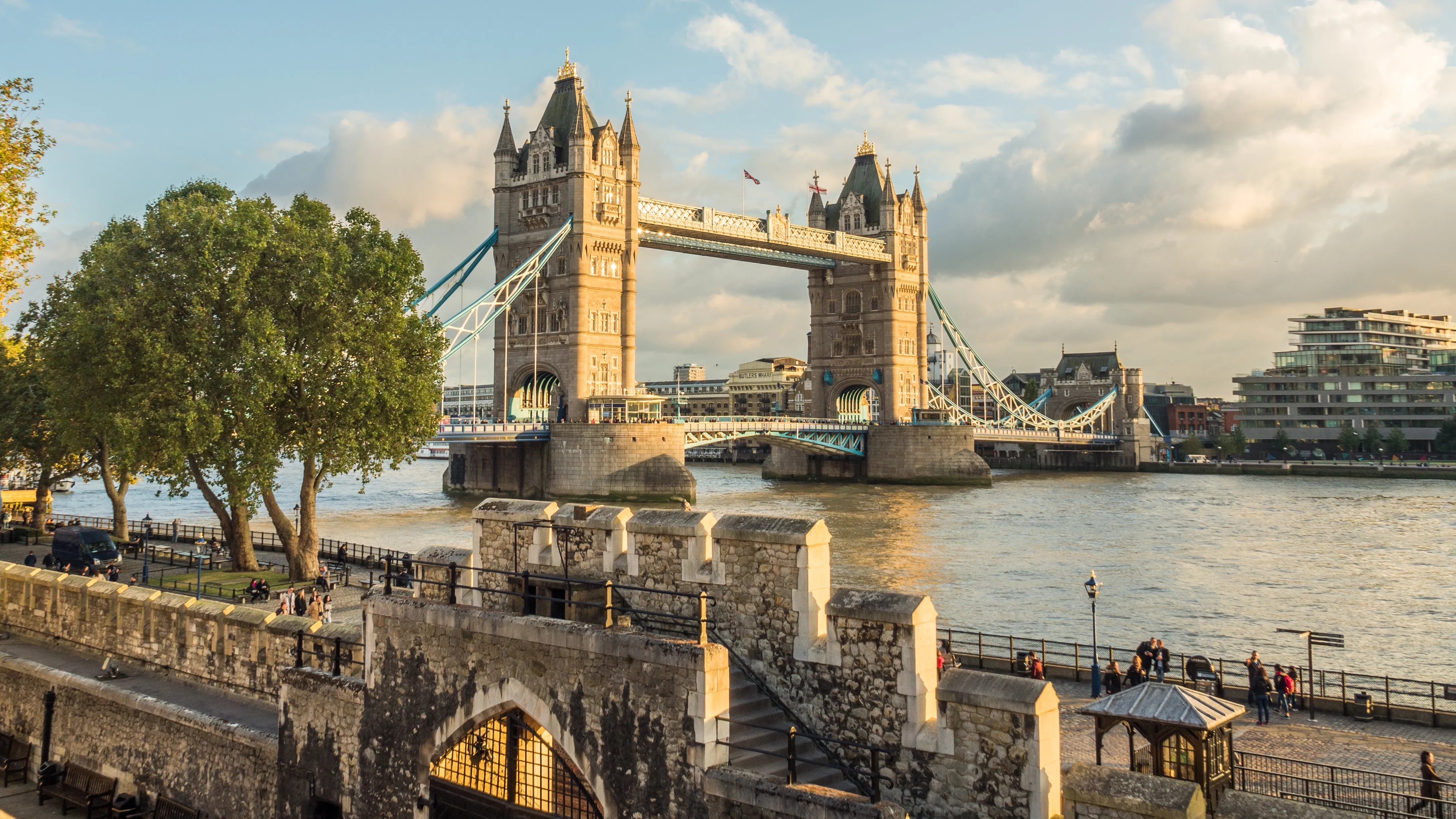 An architectural and cityscape photograph shows Tower Bridge spanning the River Thames, viewed from the historic grounds of the Tower of London, United Kingdom
