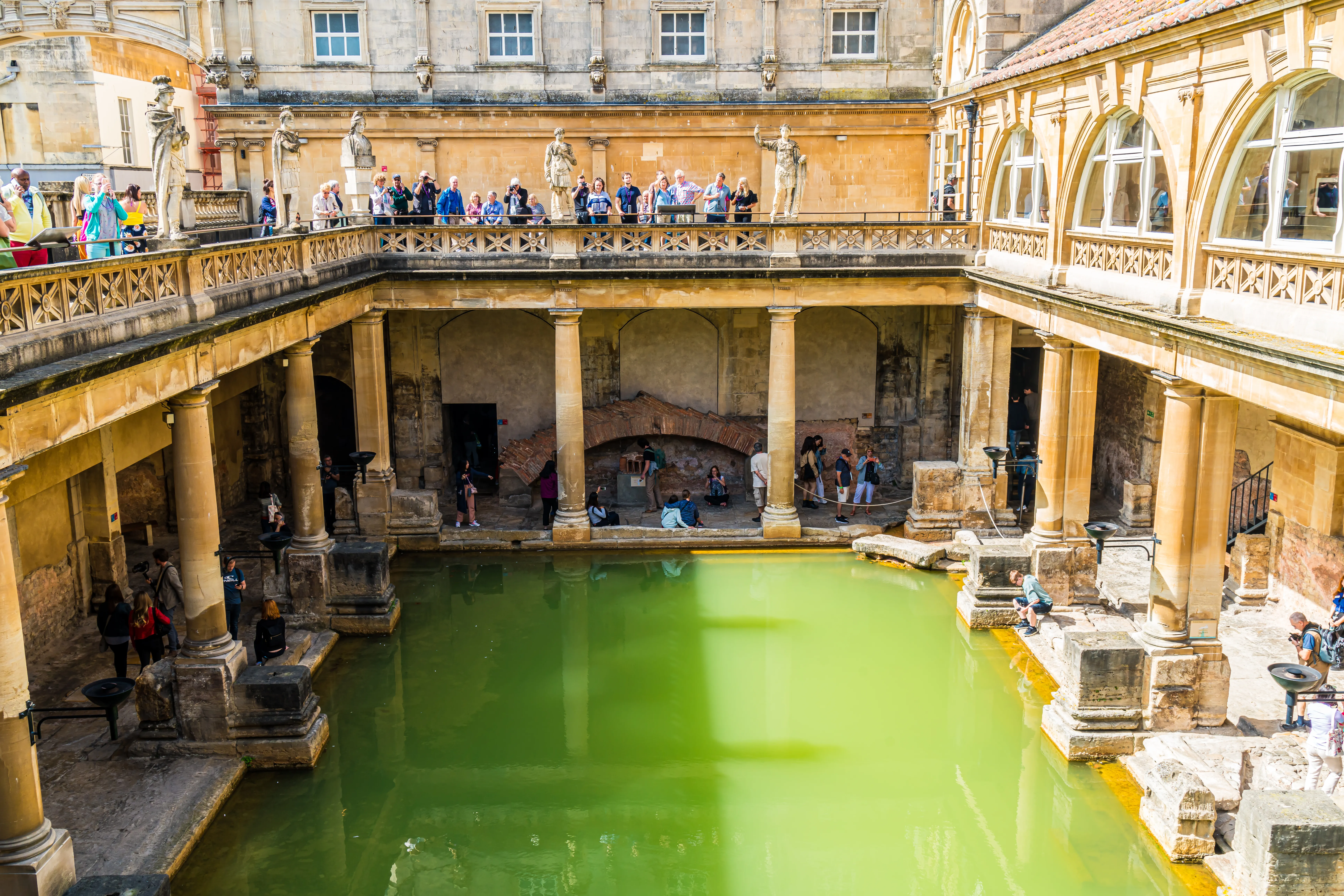 An architectural and historic photograph shows the ancient Great Bath at the Roman Baths complex in Bath, Somerset, United Kingdom