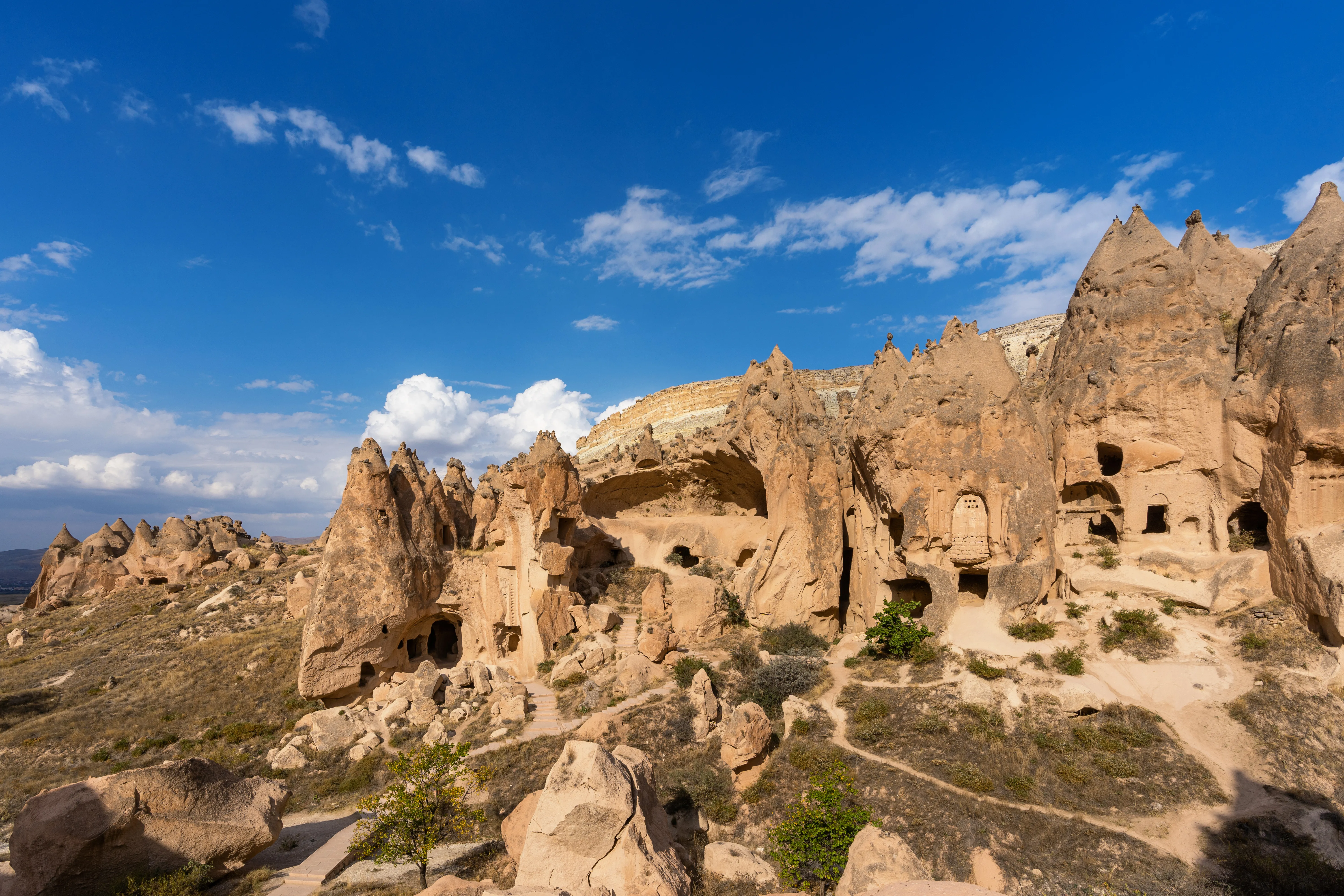 An architectural and landscape photograph shows ancient cave dwellings carved into the volcanic rock formations of Pigeon Valley in Cappadocia, Turkey.