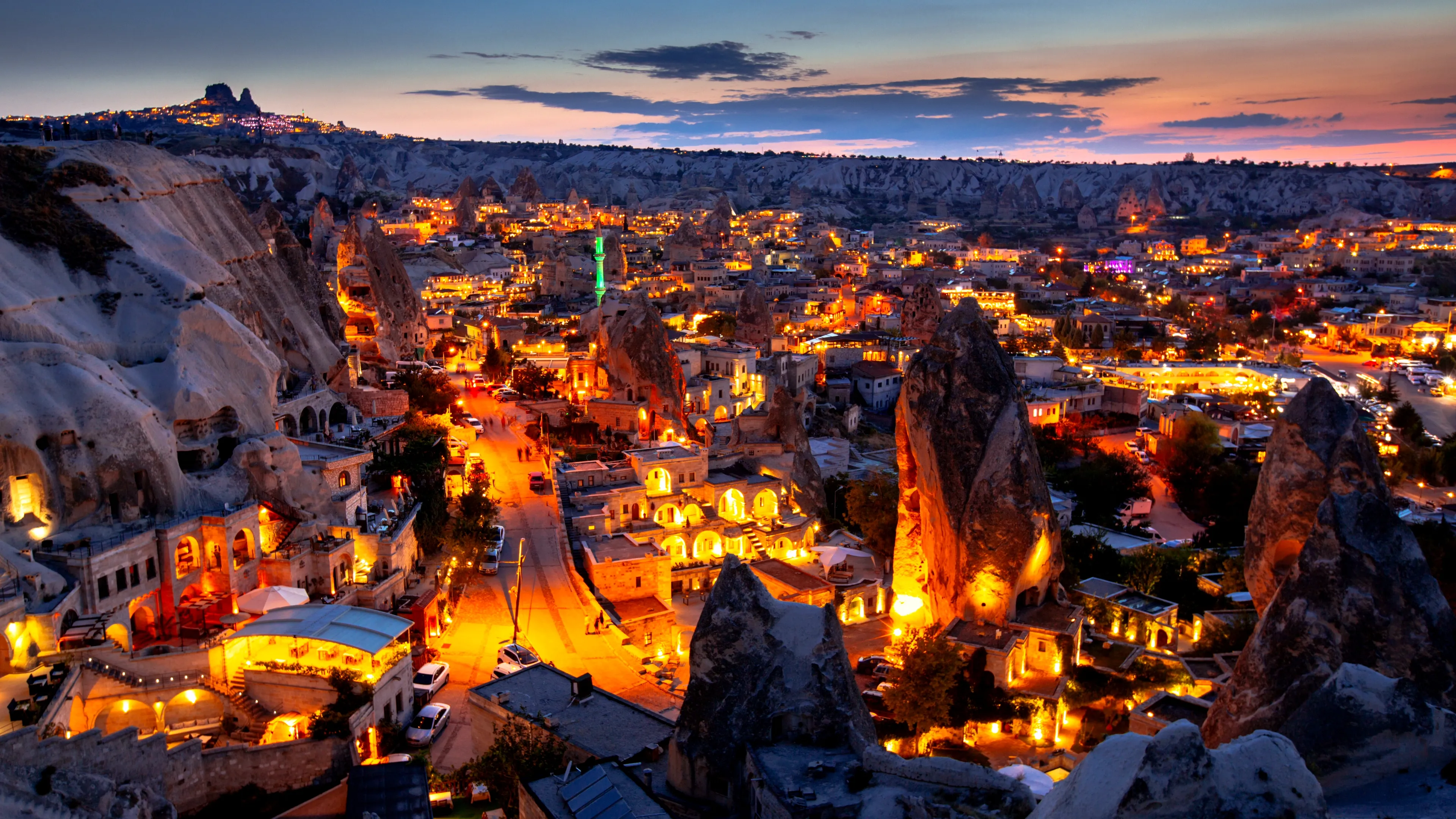 An elevated cityscape and landscape photograph shows the town of Göreme in Cappadocia, Turkey, illuminated at dusk