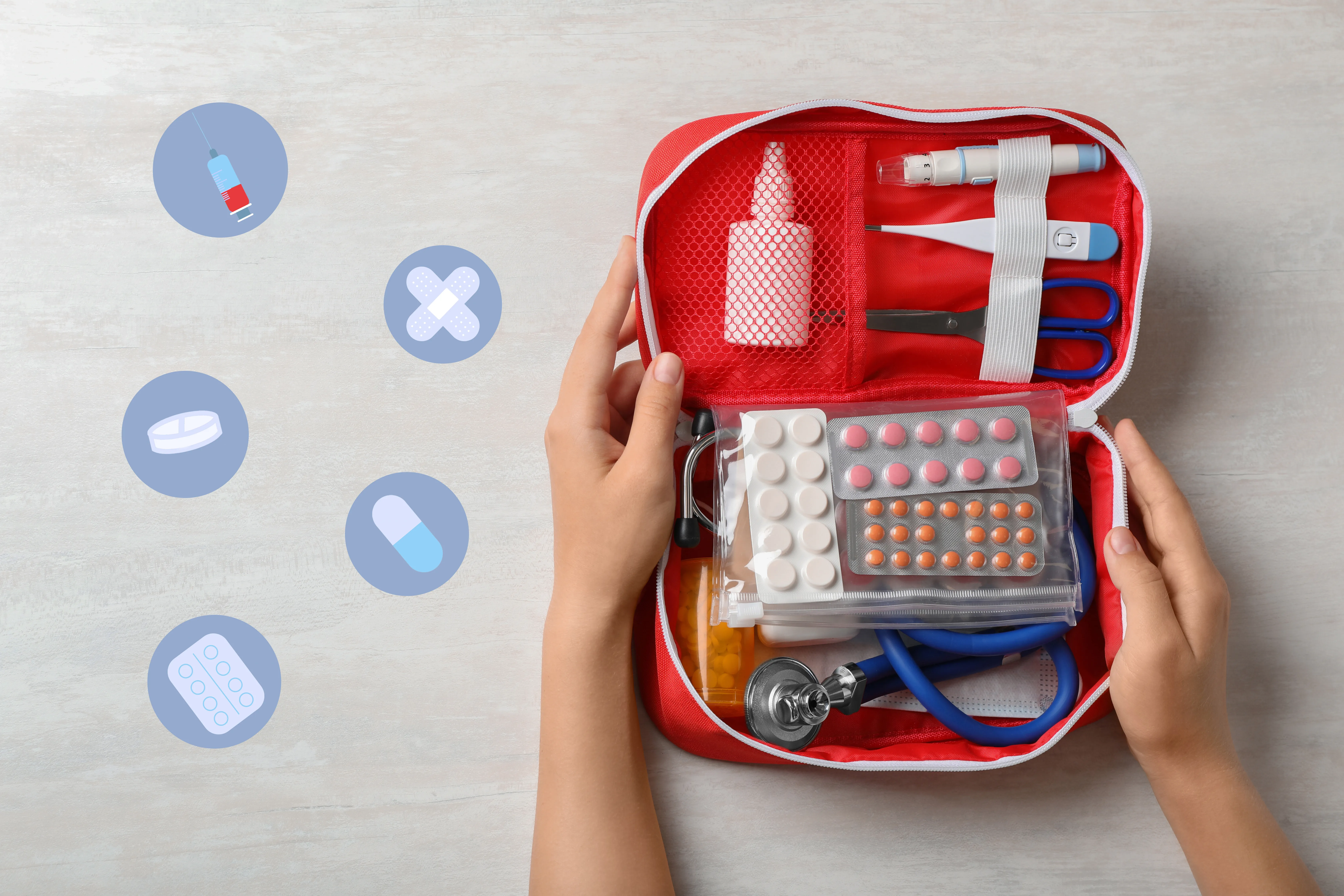An open red first aid kit filled with medical supplies and pills, held by two hands on a table