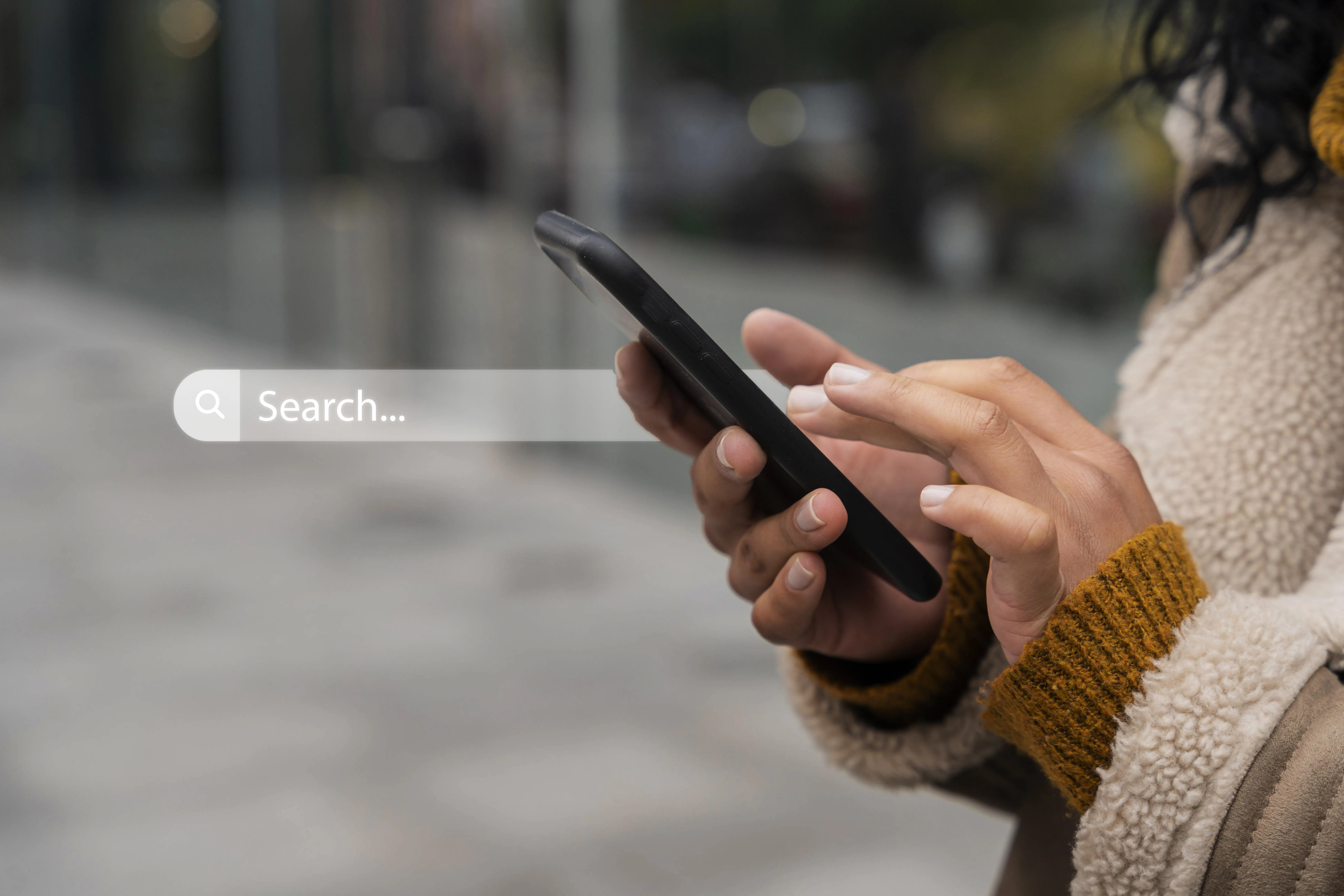 Close-up of a person typing on a smartphone outdoors with a digital search bar overlay.