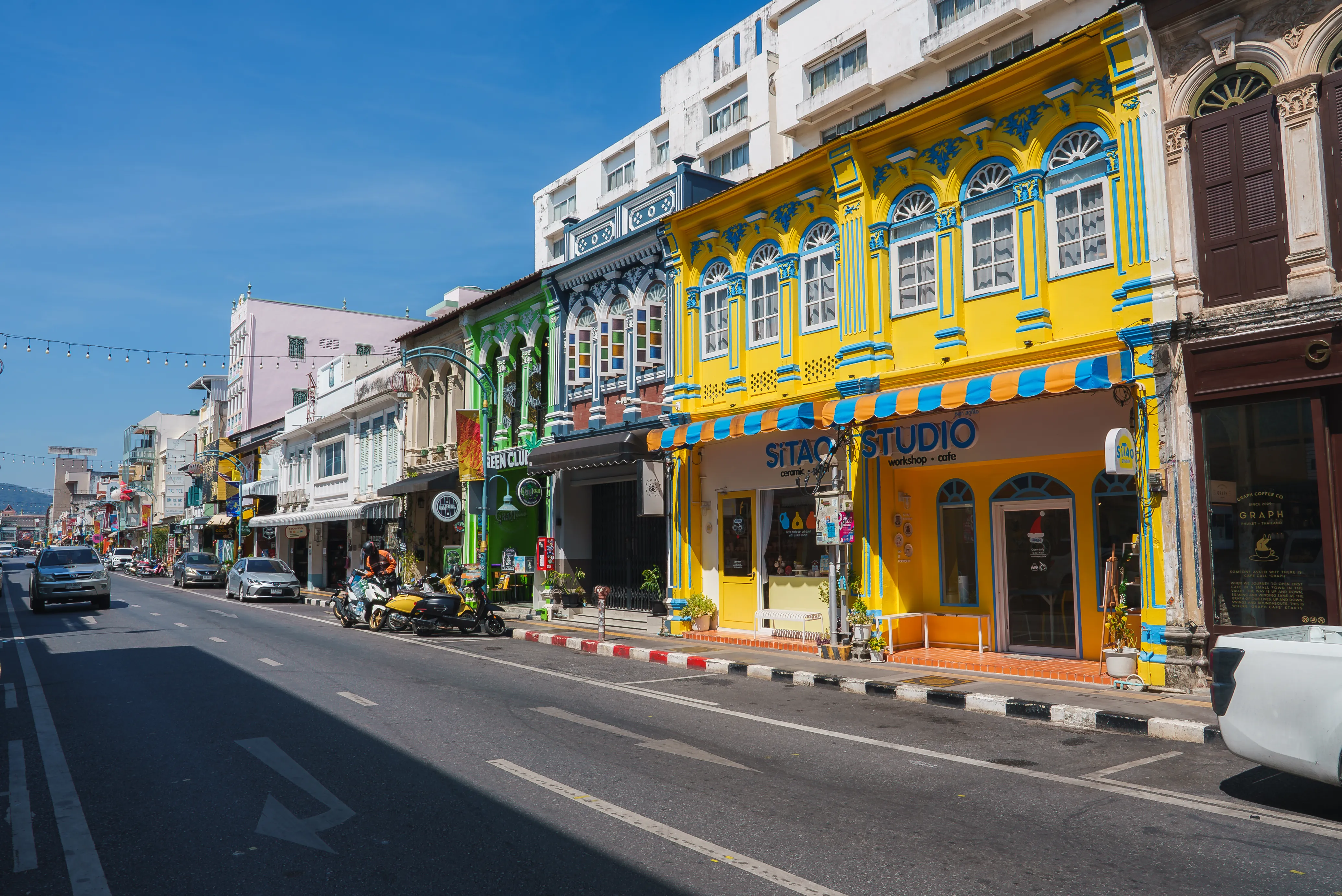  Colorful Sino-Portuguese buildings lining a street with parked motorbikes under a clear blue sky.