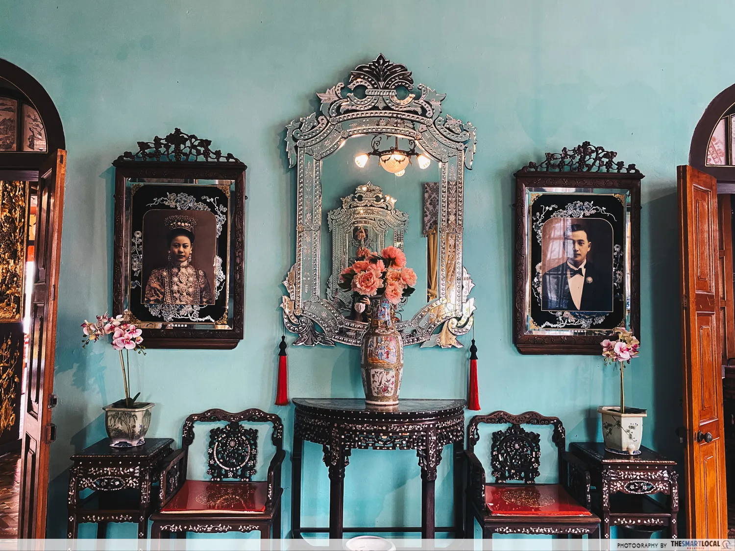 A symmetrical, eye-level shot of an opulently decorated Peranakan-style interior against a light turquoise wall.