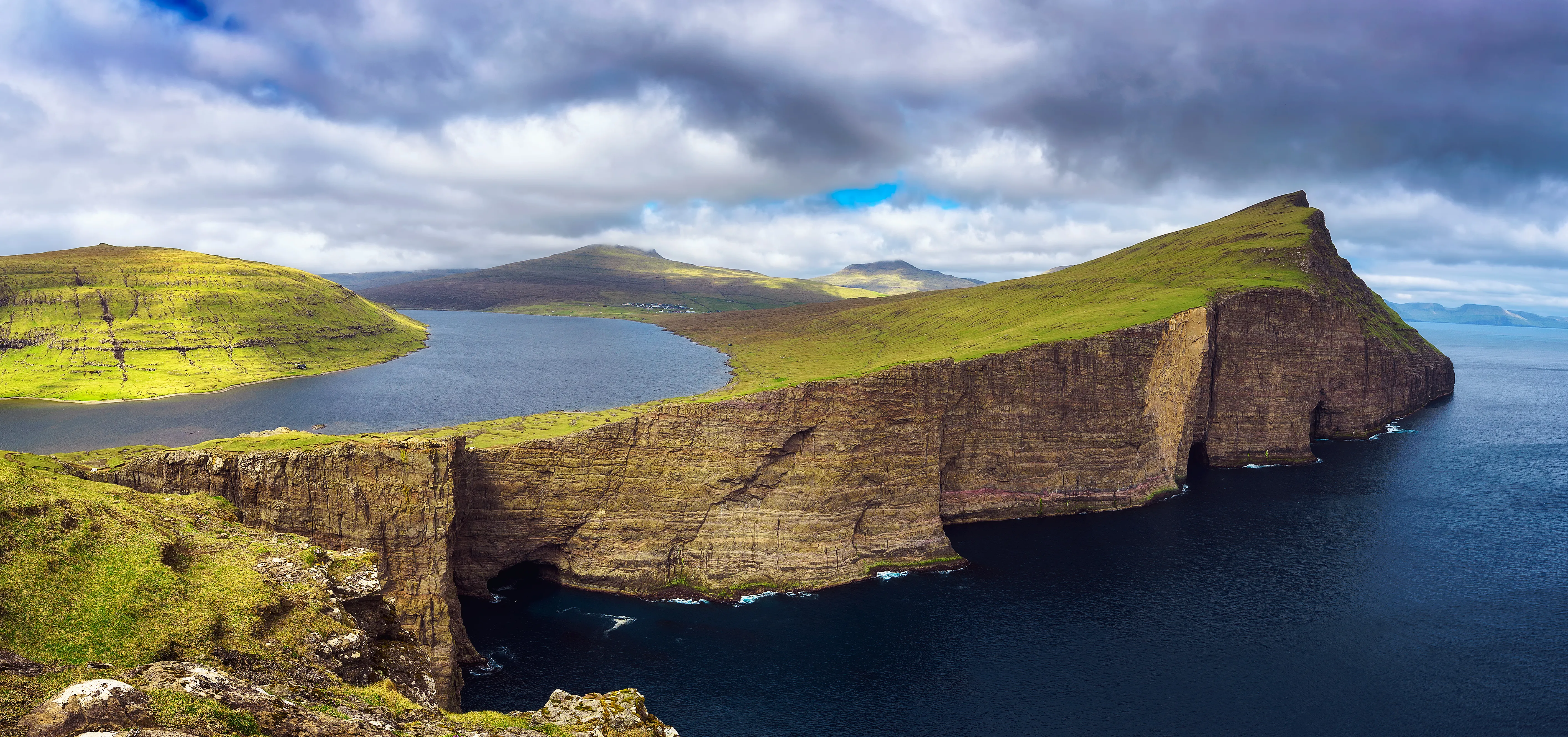 A dramatic coastal landscape featuring sheer cliffs and a tranquil lake atop a grassy plateau under a cloudy sky, evoking a sense of awe and tranquility