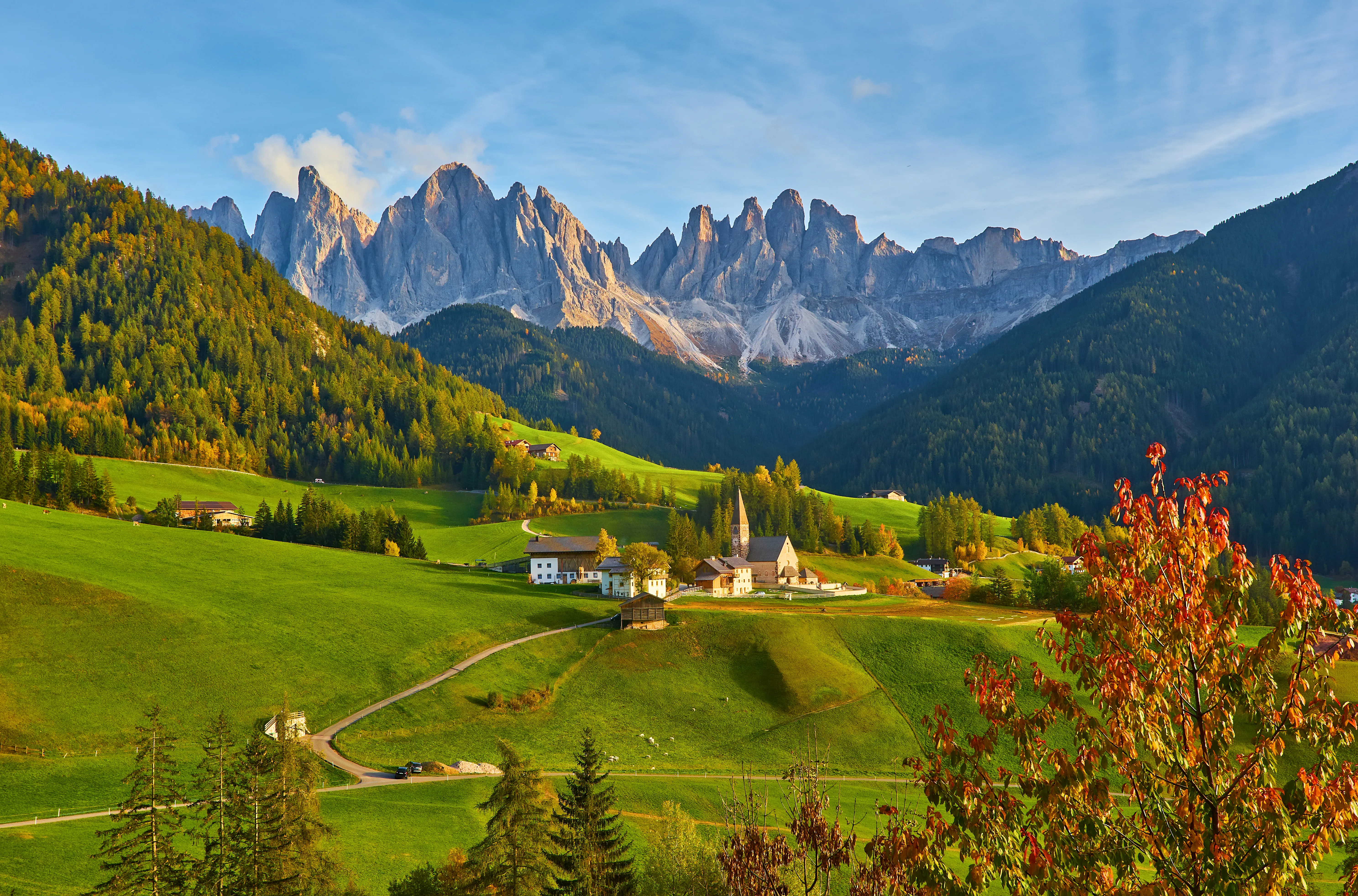 A wide-angle, eye-level shot of the picturesque village of Santa Maddalena nestled in the Val di Funes, Italy, in early autumn.