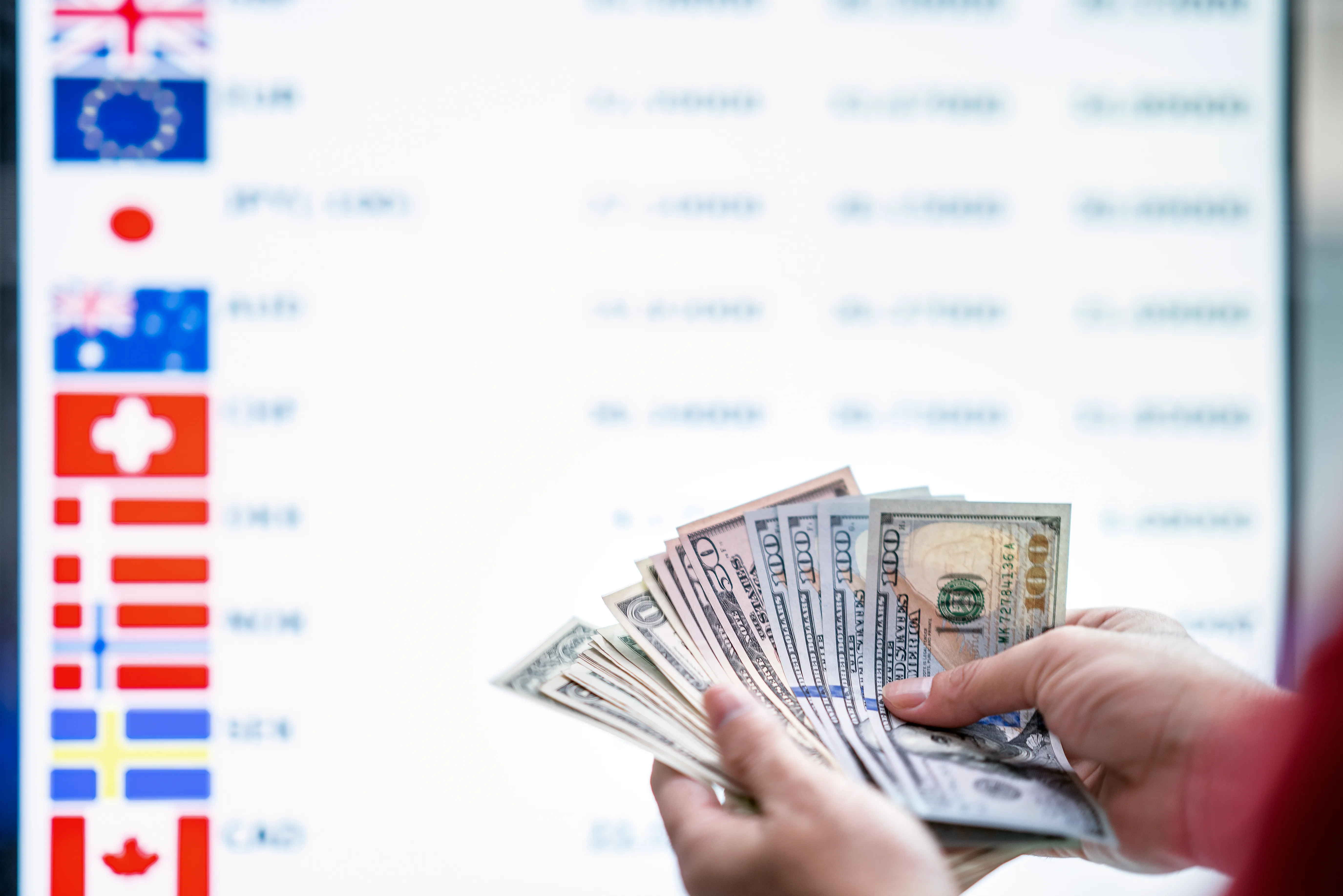 A person holds a fan of US dollars before a blurry currency exchange board.
