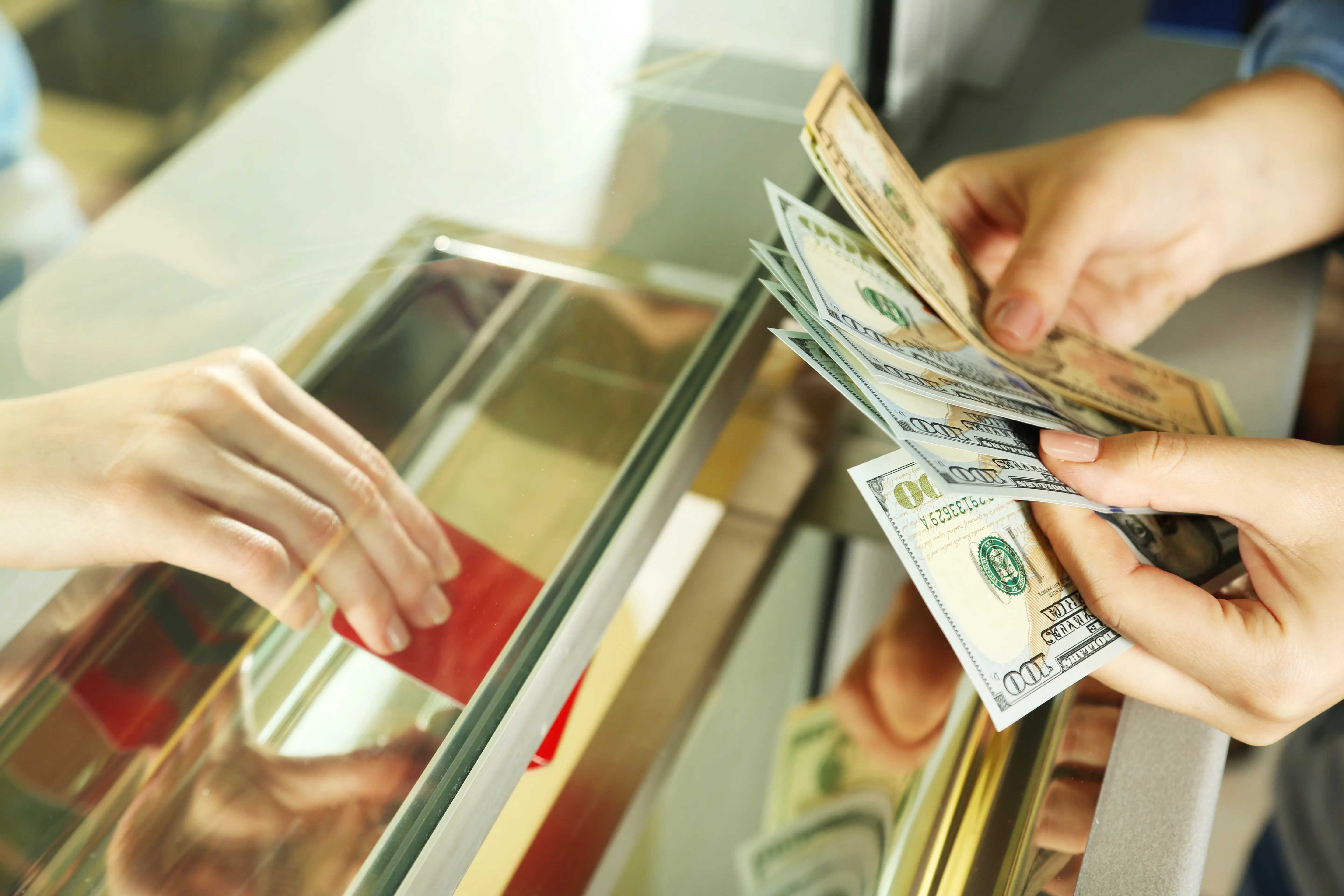 A person counts US dollar banknotes at a currency exchange or bank teller window.