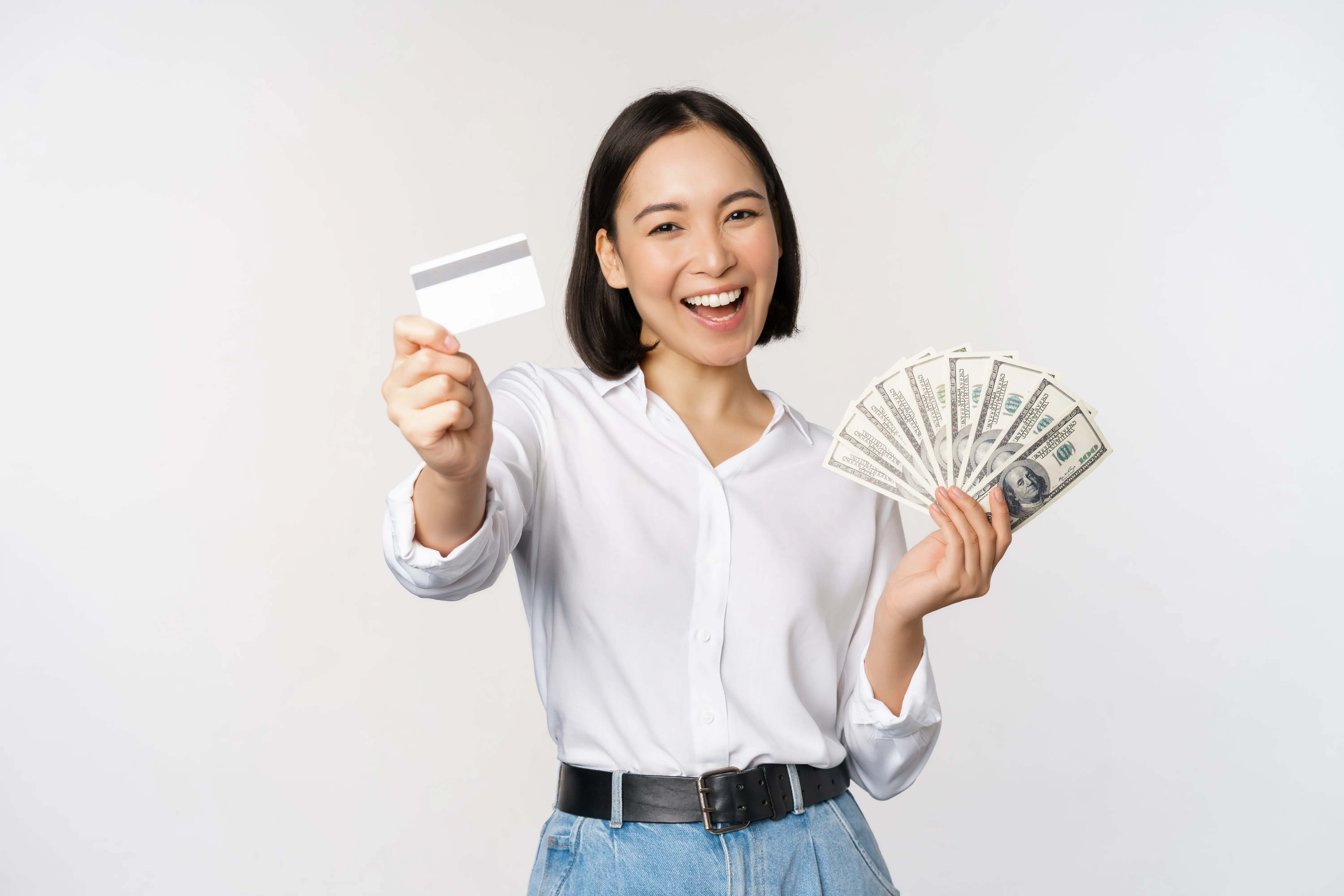 A smiling woman happily displays a white credit card and a fan of cash bills.