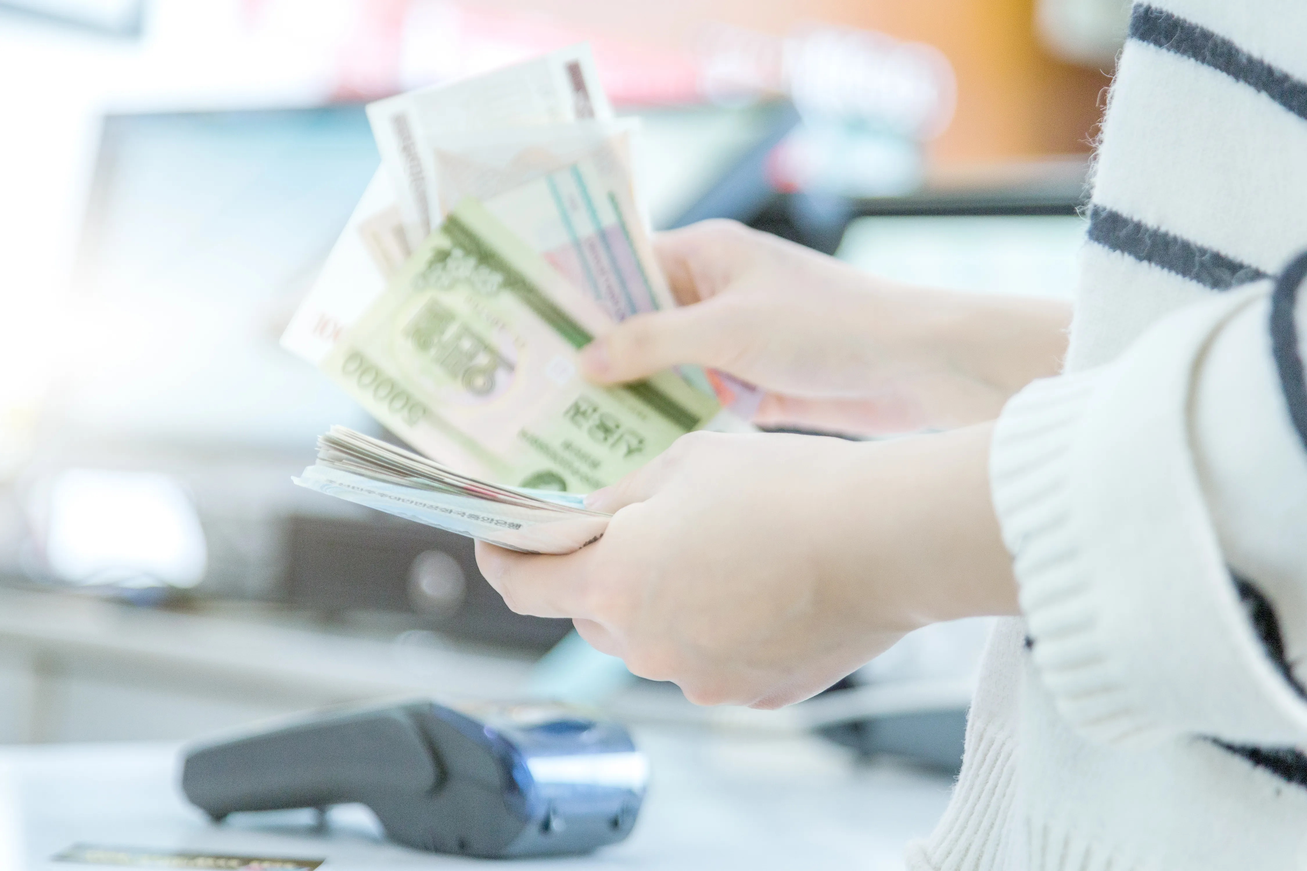 A person counts South Korean won banknotes at a checkout counter near a payment terminal.