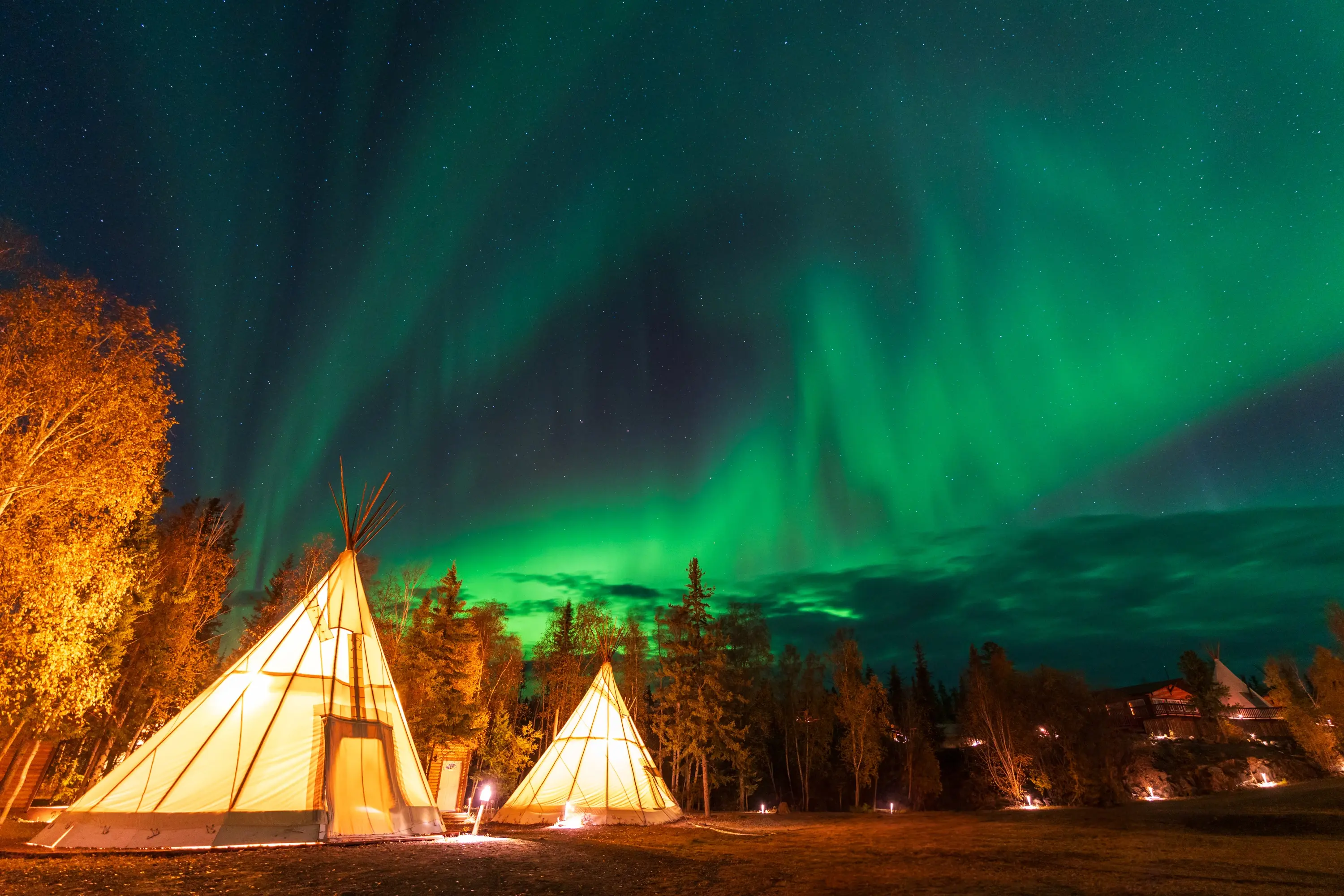 Northern Lights glowing above traditional tents in Lapland