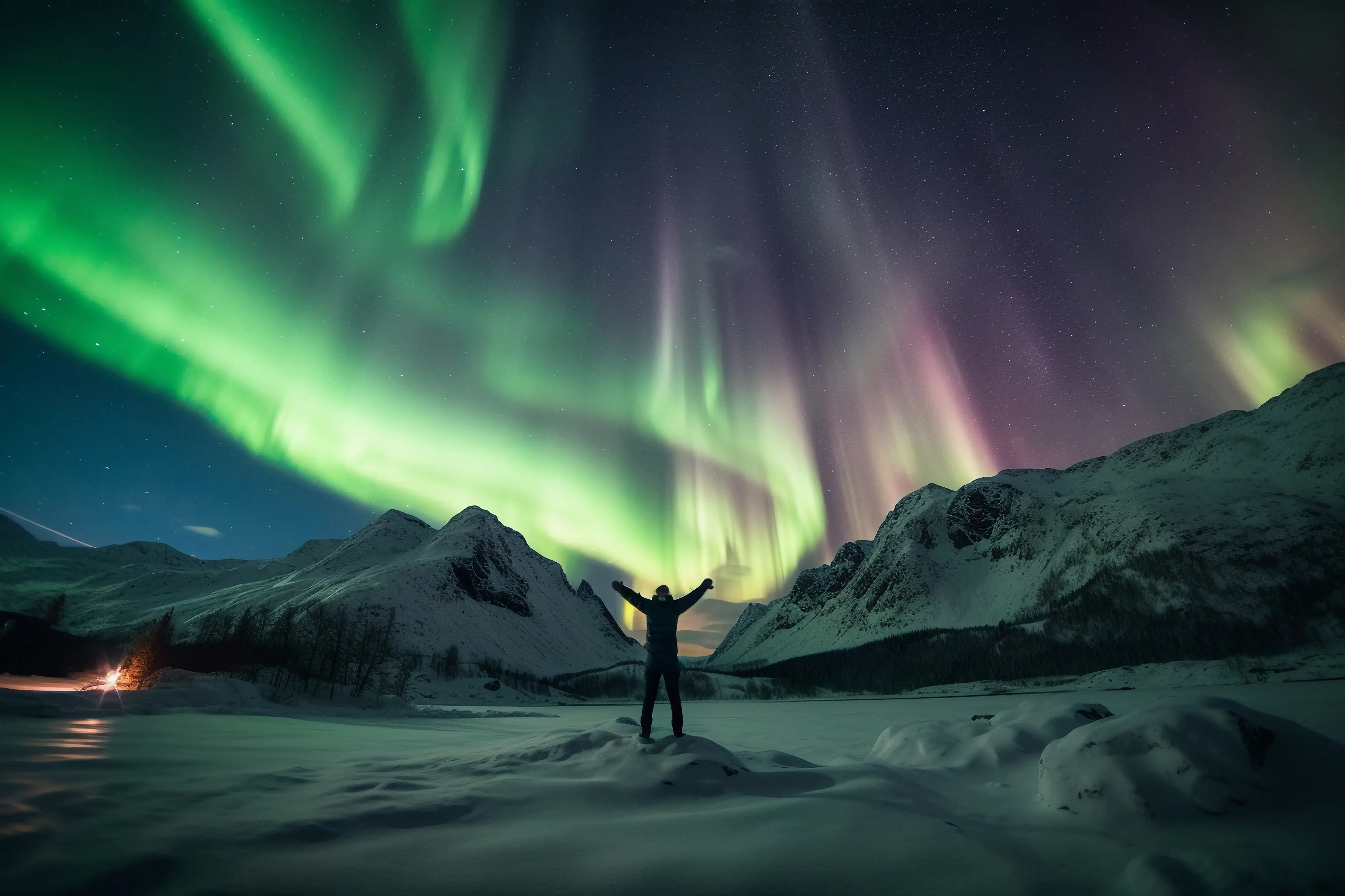 Traveler watching the Aurora Borealis over snowy mountains in Norway