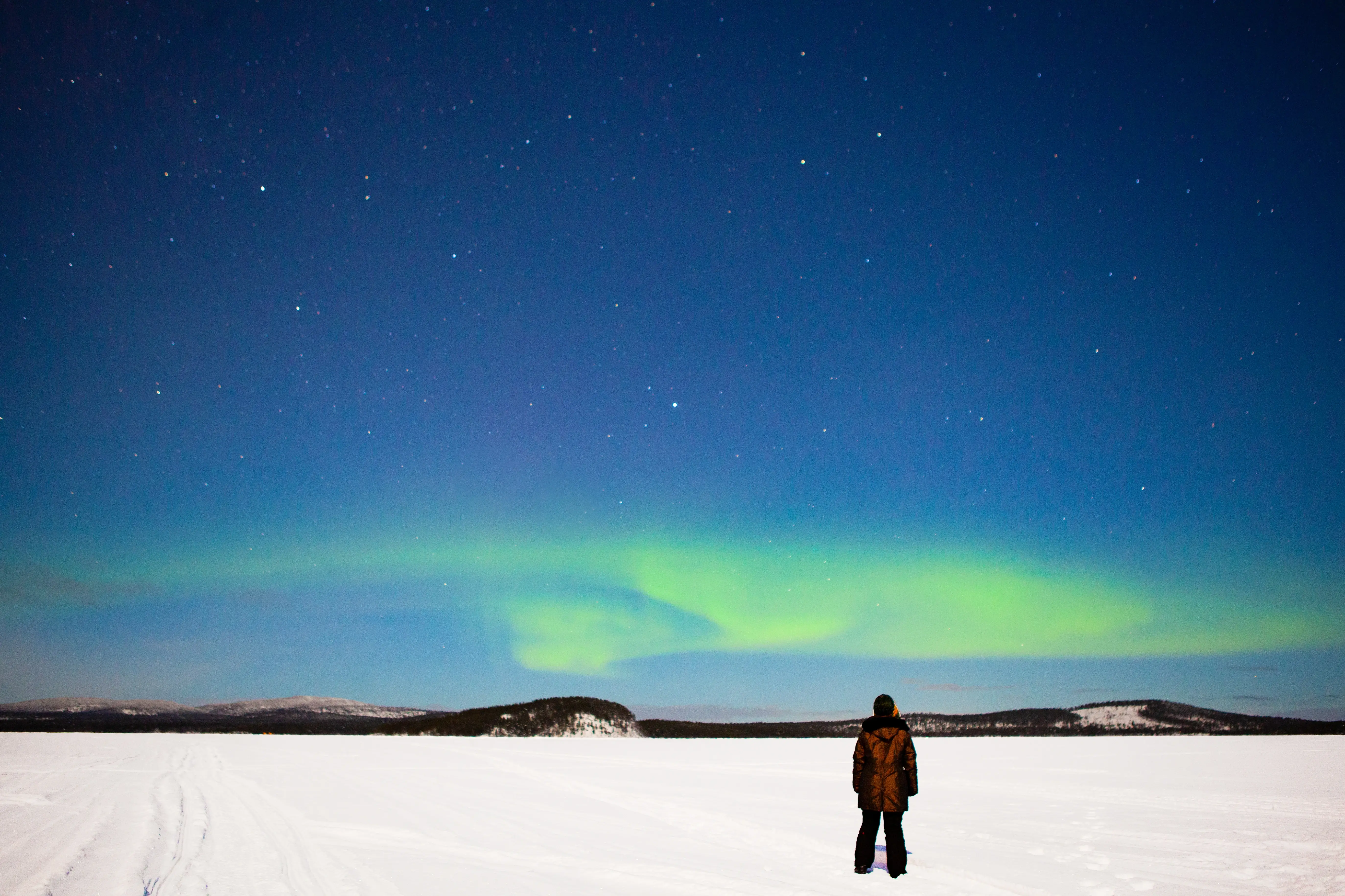 Solo traveler watching faint Northern Lights over a snowy landscape in Sweden